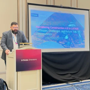 Un hombre habla desde un atril frente a una pantalla en la que se proyecta una presentación titulada «Aprovechar la Construcción 4.0 en Latinoamérica: éxitos, retos y oportunidades futuras», en un evento de Trimble Dimensions, en el que se destaca el potencial transformador de la Construcción 4.0 para la región de Latinoamérica.