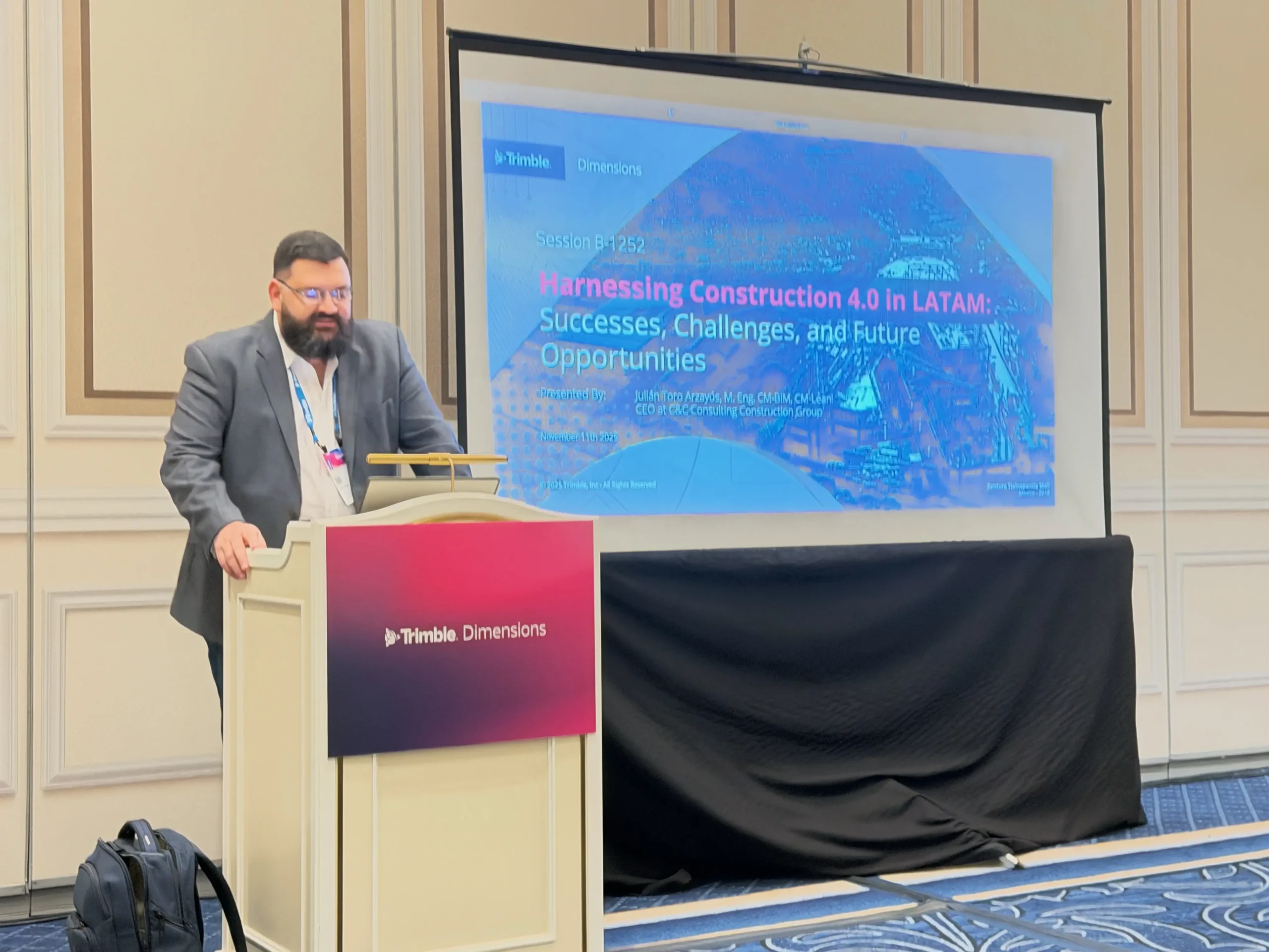 Un hombre habla desde un atril frente a una pantalla en la que se proyecta una presentación titulada «Aprovechar la Construcción 4.0 en Latinoamérica: éxitos, retos y oportunidades futuras», en un evento de Trimble Dimensions, en el que se destaca el potencial transformador de la Construcción 4.0 para la región de Latinoamérica.