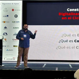 Un hombre con barba aparece en un escenario de la Expo CIHAC 2026, frente a una pantalla, hablando sobre la Construcción 4.0, con una pancarta vertical con logotipos de empresas a su izquierda.