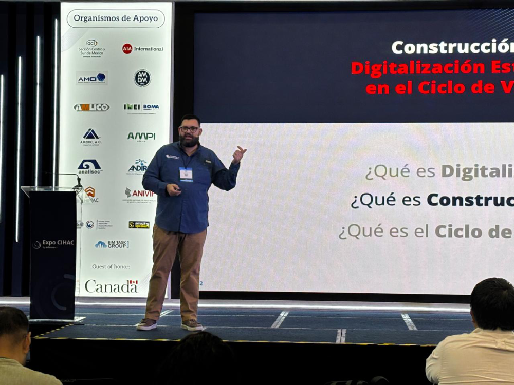 Un hombre con barba aparece en un escenario de la Expo CIHAC 2026, frente a una pantalla, hablando sobre la Construcción 4.0, con una pancarta vertical con logotipos de empresas a su izquierda.