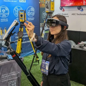 Una mujer que lleva unas gafas de realidad mixta señala con un gesto un instrumento de topografía en una feria de tecnología de la construcción.